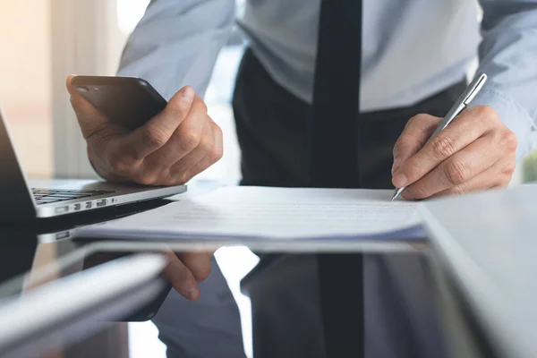 Signing contract, deal concept. Business man, executive manager working in modern office, using mobile smart phone and making a deal, signing contract, business document with laptop computer on desk, close up