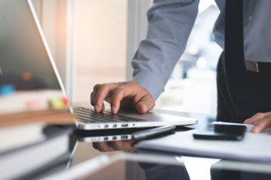 Work proceee concept. Businessman hand typing on laptop computer keyboard with business document, paperwork, digital tablet and mobile smart phone on desk. Corporate man working in office.