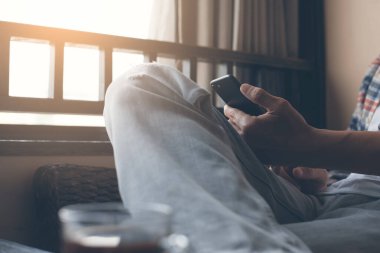 Casual business man using mobile smartphone near the window and browsing internet with a cup of coffee on table in coffee shop. Man checking internet application on phone, modern lifestyle concept