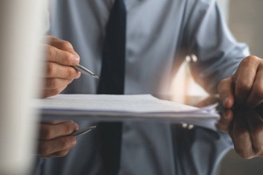 Closeup image of Businessman reading officail contract before making a deal.  Corporate man with pen in hand working in modern office, signing business document on desk. front view