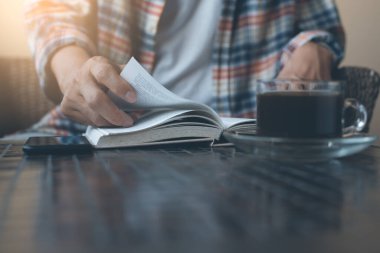 Young man opening and reading a book with a cup of coffee on table, close up, vintage style