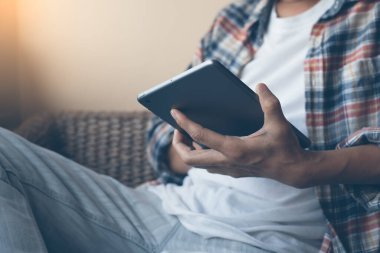 Male hipster leaning on armchair and using digital tablet computer at home