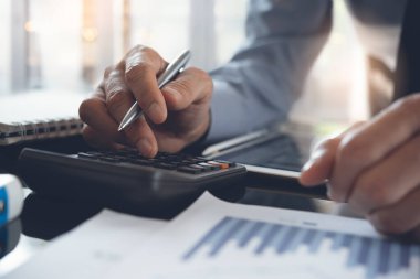 Business analysis, investment and finance concept. Business man, accountant using calculator to calculate business report, marketing data, financial graph, spreadsheet and digital tablet on office desk, close up