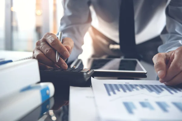 Business analysis, investment and finance concept. Business man, accountant using calculator to calculate business report, marketing data, financial graph, spreadsheet and digital tablet on office desk, close up