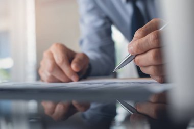 Business strategy analysis concept. Business man with pen thinking while analyzing marketing report, financial graph and working in modern office with digital tablet and spreadsheet on desk, close up