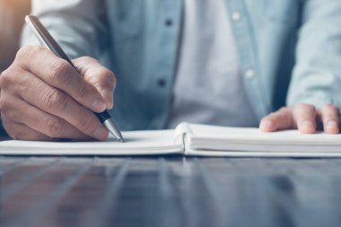 Close up of a business man writing on paper notebook with a pen