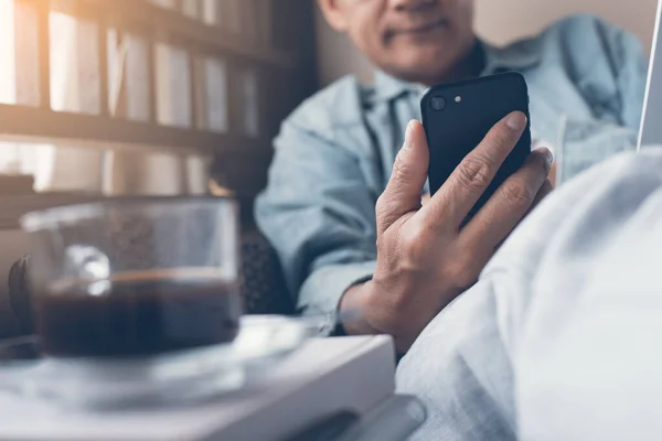 Casual businessman relaxed reading news from internet  application on mobile smartphone in the morning and using laptop computer with a cup of coffee on table at home, internet of things IoT concept, close up