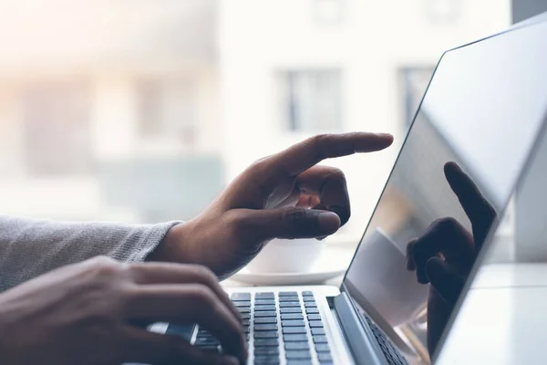 Casual business man working on laptop computer and pointing at the screen with coffee cup on office desk, morning light, close up man working at home office.