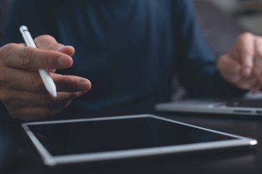 Website designer with stylus pen working digital tablet and computer laptop on wooden desk. Casual business man hand touching on touchpad screen, close up. Freelance online working from home, close up