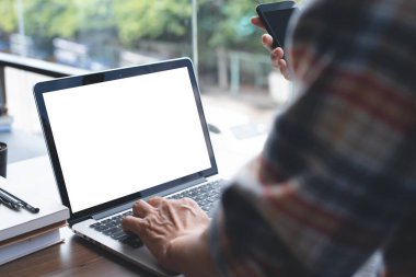 Mock up image of casual man working on laptop computer and using mobile smart phone in coffee shop