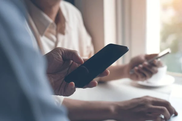 Two men friends or colleagues meeting in a coffee shop and using mobile smartphone, browsing website on phone, social media communication, e business, internet payment, internet of things IoT concept