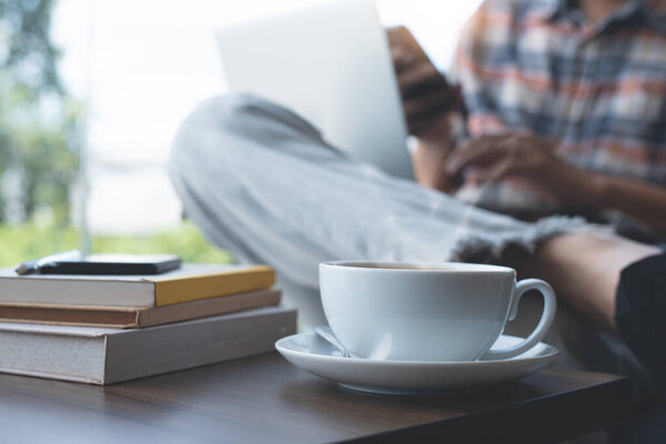 Casual man, hipster, freelance using mobile smart phone, working on laptop computer with cup of coffee and books on wodden table at coffee shop. Online working, portable office concept