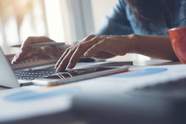 Cropped, smart  businesswoman, entrepreneur working on laptop computer in modern office with smartphone, cup of coffee, calculator and business data report on desk