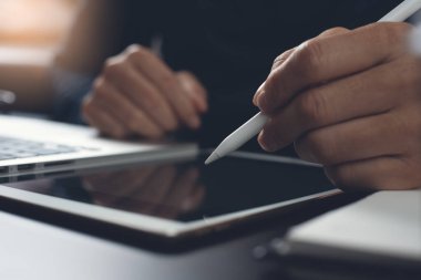 Casual man, freelance with stylus pen writing on digital tablet screen, working on laptop computer with notebook on office desk. Graphic or web designer plnning his work project, dark tone, close up. Startup business, technology concept