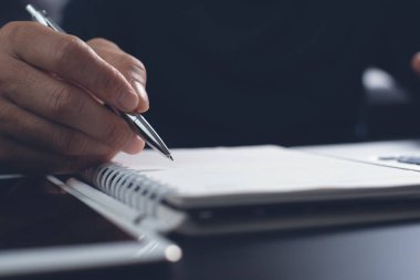 E-learning, online education. Student writing content on paper notebook with a pen while studying online course via laptop computer with digital tablet on desk. Business man planning work on notepad in office. Startup business, close up