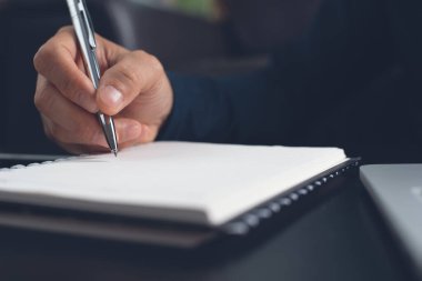 E-learning, online education. Student writing content on paper notebook with a pen while studying online course via laptop computer with digital tablet on desk. Business man planning work on notepad in office. Startup business, close up