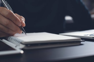 E-learning, online education. Student writing content on paper notebook with a pen while studying online course via laptop computer with digital tablet on desk. Business man planning work on notepad in office. Startup business, close up
