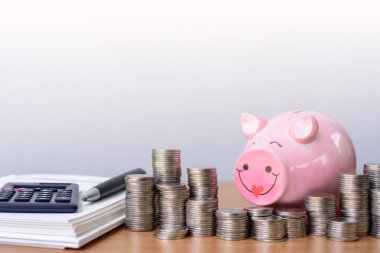 Happy piggybank and tower of coins, money tower, calculator and notebook on wooden table, money saving concept.