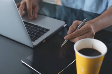 Casual business man, designer, freelance holding pen while working on laptop computer with digital tablet and cup of coffee on desk in office, startup business and modern technology concept