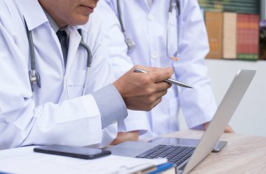 Medical teamwork concept. Two doctors having discussion about patient diagnosis on laptop computer with smart phone and book on desk in hospital.