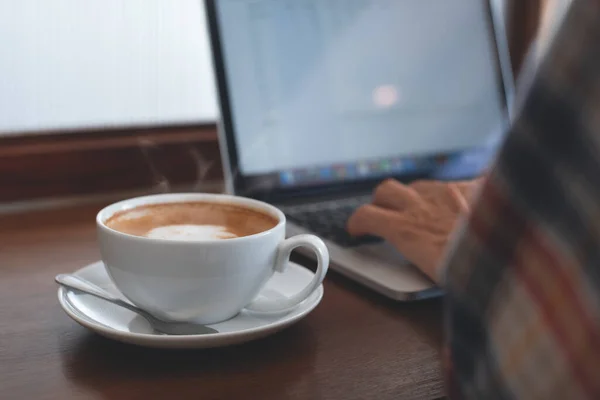 Casual business man, hipster, freelance browsing internet on laptop computer with cup of coffee, mobile smartphone on wodden table at coffee shop with copy space. portable office concept, vintage style