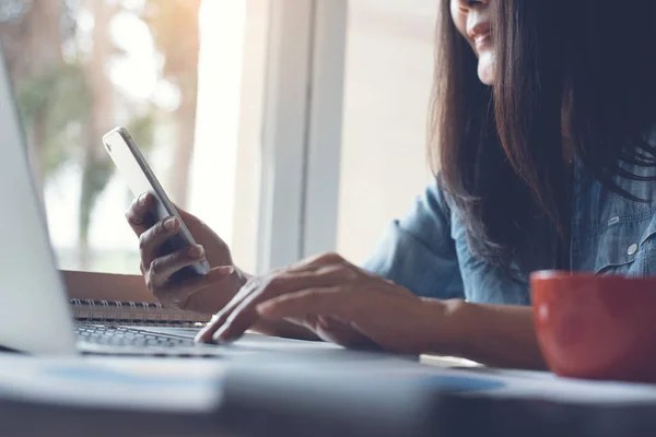 Cropped, smart  businesswoman, entrepreneur using smart phone, working on laptop computer in modern office with cup of coffee, calculator, books and business data report on desk