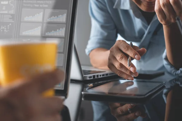 Business analysis and modern technology concept. Businessman and teamwork analyzing business data, marketing report monitoring on laptop computer and  digital tablet on desk in office.