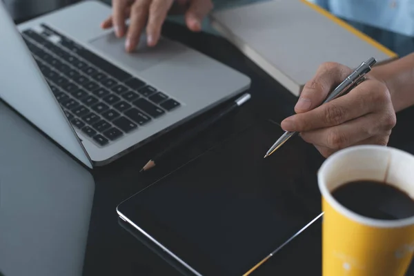 Casual business man, designer, freelance holding pen while working on laptop computer with digital tablet and cup of coffee on desk in office, startup business and modern technology concept