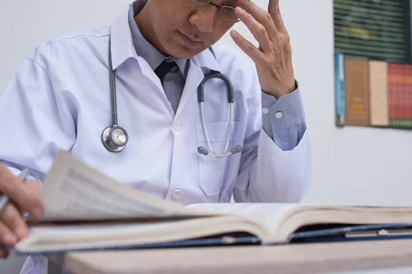 Asian doctor concentrate reading  textbook for medical research, close up. Selective focus on stethoscope.