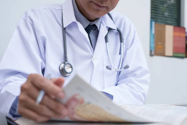 Cropped image, male doctor reading anatomy textbook. Medical sudent reading book in medical school, health education concept