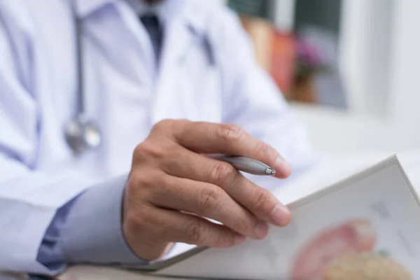 Cropped image, male doctor reading anatomy textbook. Medical sudent reading book in medical school, education concept, selective focus on tip of pen