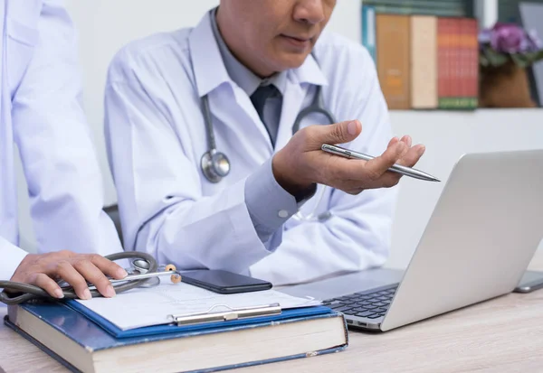 Medical teamwork concept. Two doctors having discussion about patient diagnosis on laptop computer with smart phone and book on desk in hospital.