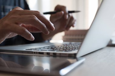 Casual businessman or freelancer busy working on laptop computer and digital tablet, holding a pen in office. Man, entrepreneur online working at home office, close up