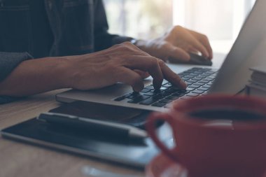 Casual businessman, freelancer working on laptop computer. Man browsing internet with cup of coffee, mobile smart phone, digital tablet on desk, online working from home office, vintage tone..