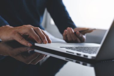 Akıllı cep telefonu ve dizüstü bilgisayar kullanarak evden çalışan genç bir adam. Sıradan bir iş adamı iş yerinde mobil uygulamayı kontrol ediyor. Çevrimiçi çalışma, taşınabilir ofis konsepti, klasik ton