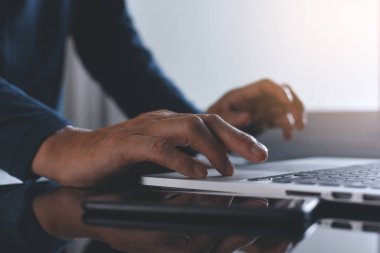 Evdeki cep telefonuyla dizüstü bilgisayarda çalışan sıradan bir adamın görüntüsü. Evden bağımsız çalışma, taşınabilir ofis kavramı