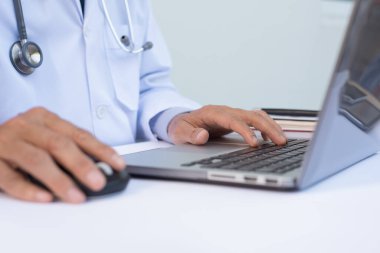 Bilgisayarda çalışan erkek doktoru kapatın hastanedeki beyaz masada, elektronik sağlık kayıt sistemi EHR 'ler, elektronik tıbbi kayıt sistemleri EMR' ler, teletıp konsepti, seçici odaklanma.