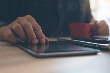 Kahve içen, dijital tablet bilgisayar kullanan, bilgisayarla çalışan, ahşap masada akıllı telefonları olan, internet bankacılığı yapan, e-kitap konsepti olan bir adam.