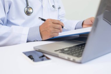 Hasta sağlık raporlarına yazı yazan ve hastanedeki beyaz masada telif alanı, elektronik sağlık kayıt sistemi EHR, telekonferans veya teletıp konsepti olan dizüstü bilgisayar üzerinde çalışan erkek doktorların kapatılması.