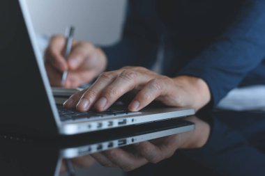 Evdeki masada yansıması olan sıradan bir adamın dizüstü bilgisayarda çalışırken çekilmiş görüntüsü. Evden bağımsız çalışma, taşınabilir ofis konsepti, kapatma