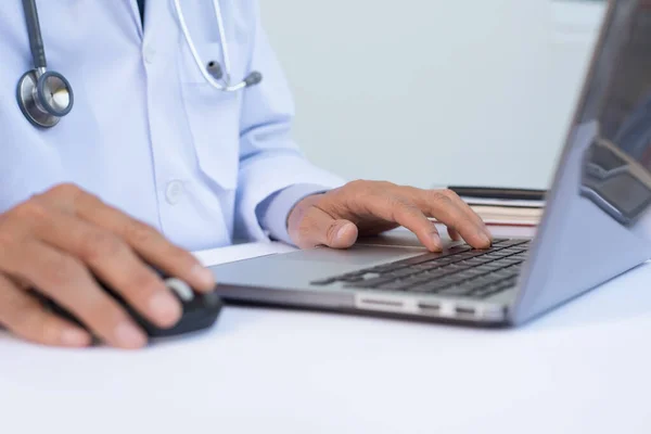 Close up of male doctor working on laptop computer on white desk in hospital, electronic health records system EHRs, electronic medical records system EMRs, telemedicine concept, selective focus.