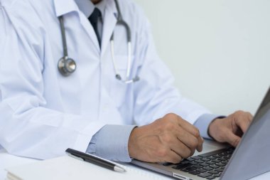 Telif alanı, elektronik sağlık kayıt sistemi EHR, telekonferans ya da teletıp konsepti olan hastanedeki beyaz masadaki dizüstü bilgisayarda çalışan erkek doktorların kapatılması.
