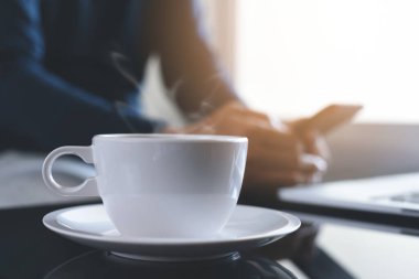 Bir fincan sıcak kahve ve sigara, sıradan bir adamla masanın üzerinde cep telefonu ve dizüstü bilgisayarla sabah güneşiyle birlikte çalışma, kopyalama alanı.