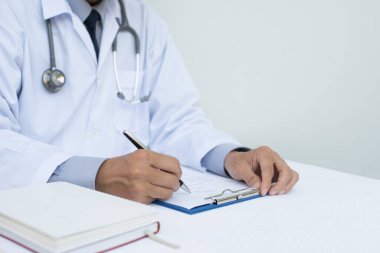 Hasta dosyasını panoya siyah kalemle dolduran erkek doktoru hastane masasında beyaz kalemle kapatın..