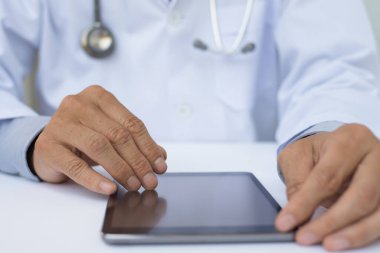 Steteskoplu erkek doktor ya da tıp öğrencisinin hastanedeki beyaz masadaki boş tablet bilgisayara fotokopi cihazıyla dokunuşunu kapat..