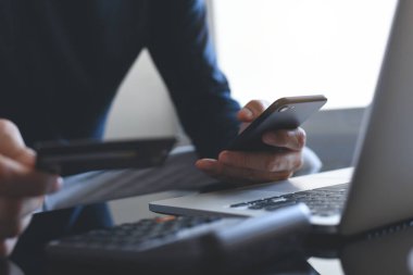 Çevrimiçi ödeme, dijital bankacılık. Akıllı cep telefonunu elinde tutan bir adam, online alışveriş için kredi kartı kullanıyor. Bilgisayarlı ve tabletli. Siber pazartesi konsepti