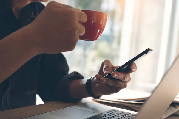 Sıradan bir iş adamı, cep telefonu kullanan, kahve içen, ev ofisinin penceresinin yanındaki bilgisayarda sabah güneşiyle çalışan serbest çalışan,