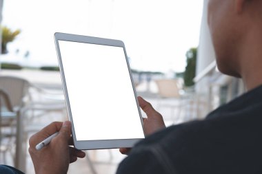 Beyaz dijital tablet ve beyaz ekranlı stilus kalem tutan bir adamın görüntüsünü taklit et. Kafede oturanları arka plan olarak bulanıklaştır. omuz görünümü