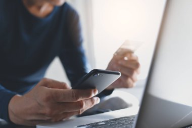 Çevrimiçi ödeme, dijital bankacılık. Akıllı cep telefonunu elinde tutan bir adam, online alışveriş için kredi kartı kullanıyor. Bilgisayarlı ve tabletli. Siber pazartesi konsepti