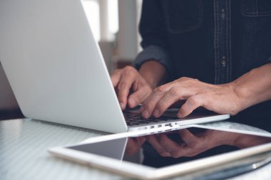 Online working from home, portable office, freelance lifestyle concept. Casual business man, freelancer connecting internet, working on laptop computer with digital tablet on desk at home or coffee shop, close up